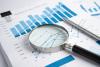 close up image of pile of paper with charts and graphs and a magnifying glass laying on top